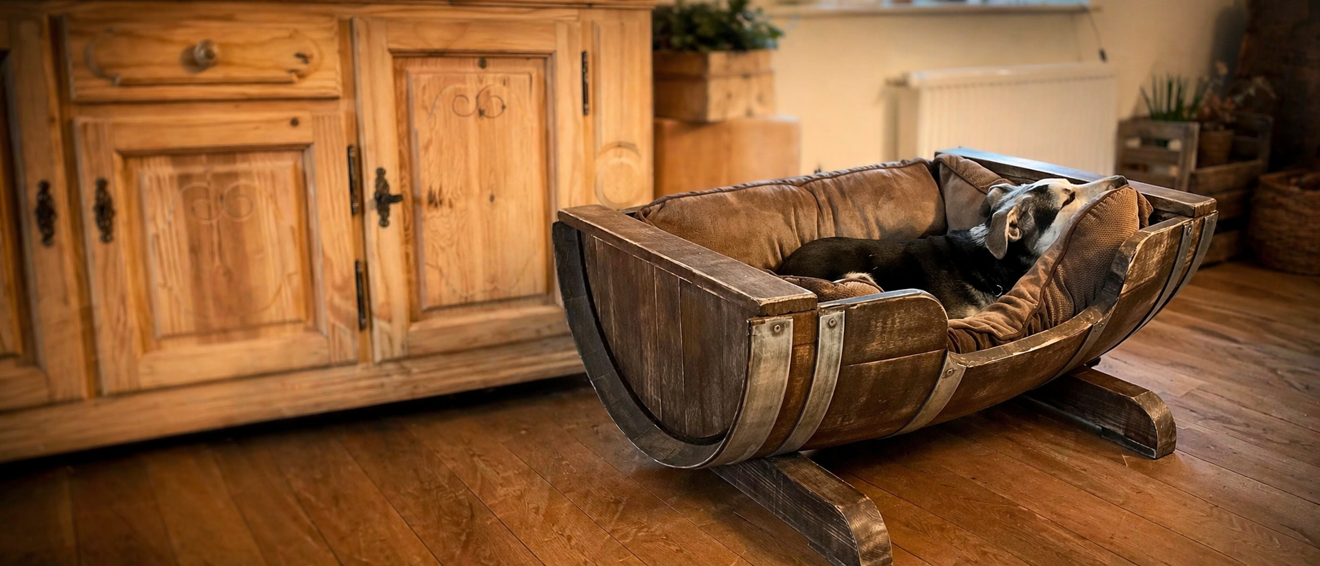Hund schläft entspannt in handgefertigtem Hundebett aus einem recycelten Weinfass vor rustikalem Holzschrank in wohnlicher Umgebung