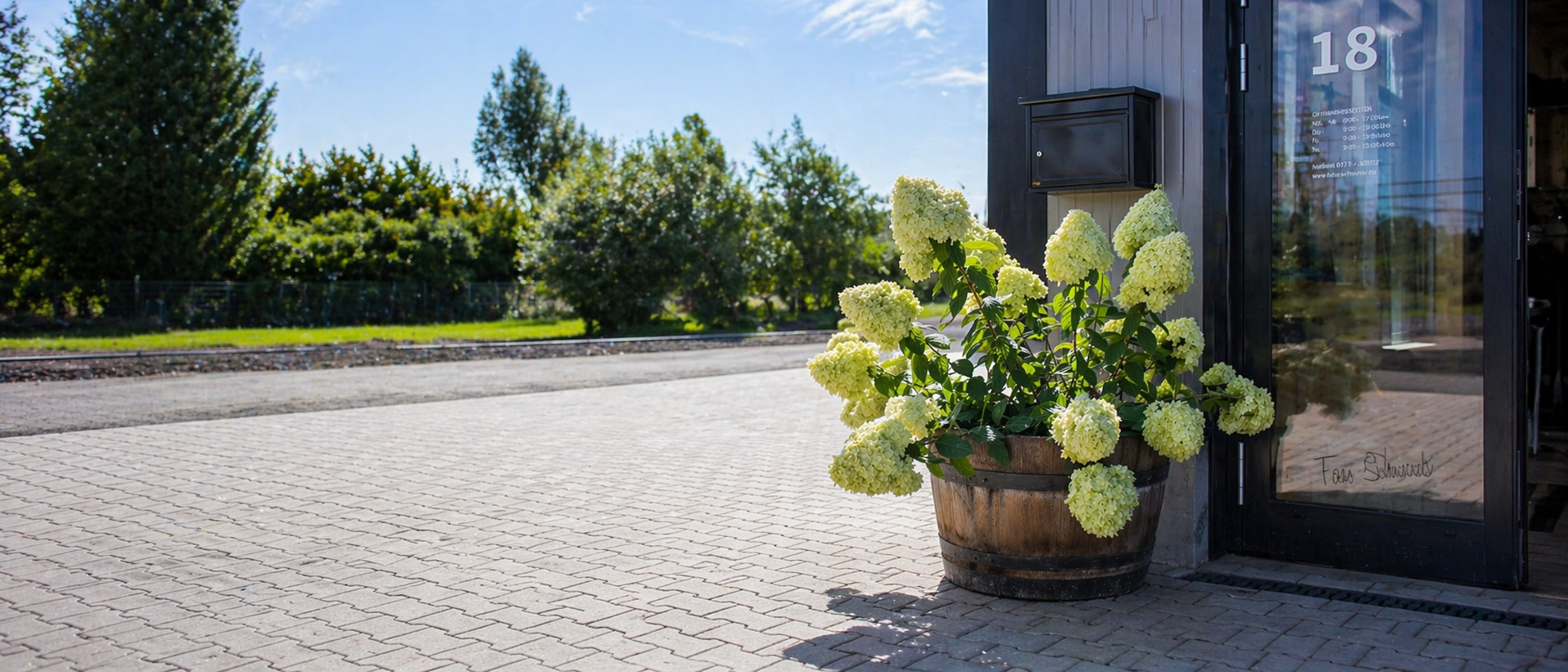 Pflanzkübel aus recyceltem Weinfass mit blühender Hortensie vor modernem Eingang, auf Pflastersteinen mit Freifläche links – handgefertigte Holzfass-Dekoration im Außenbereich