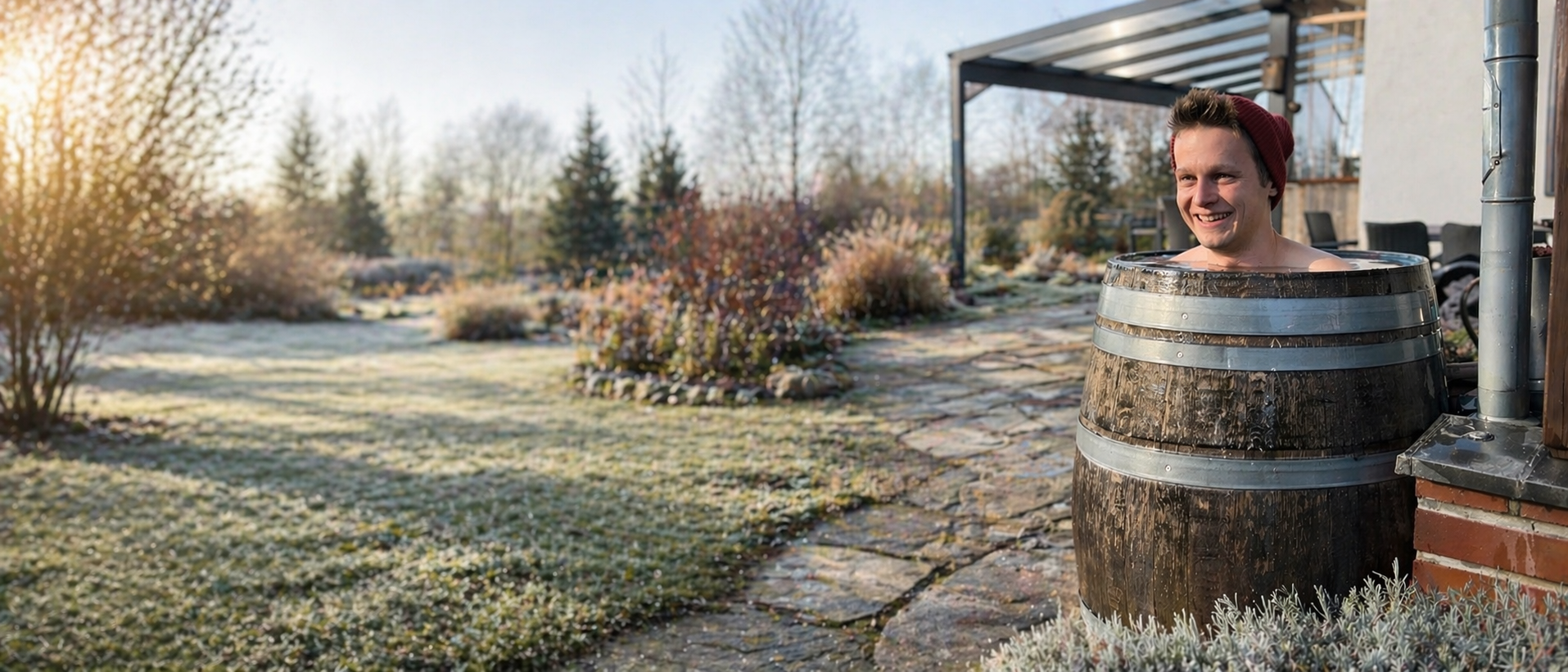 Junger Mann entspannt sich in einem hölzernen Weinfass im Garten, rechts im Bild positioniert; links ein weichgezeichneter, ruhiger Frühlingsgarten mit Rasen, Sträuchern und Bäumen im Morgenlicht.