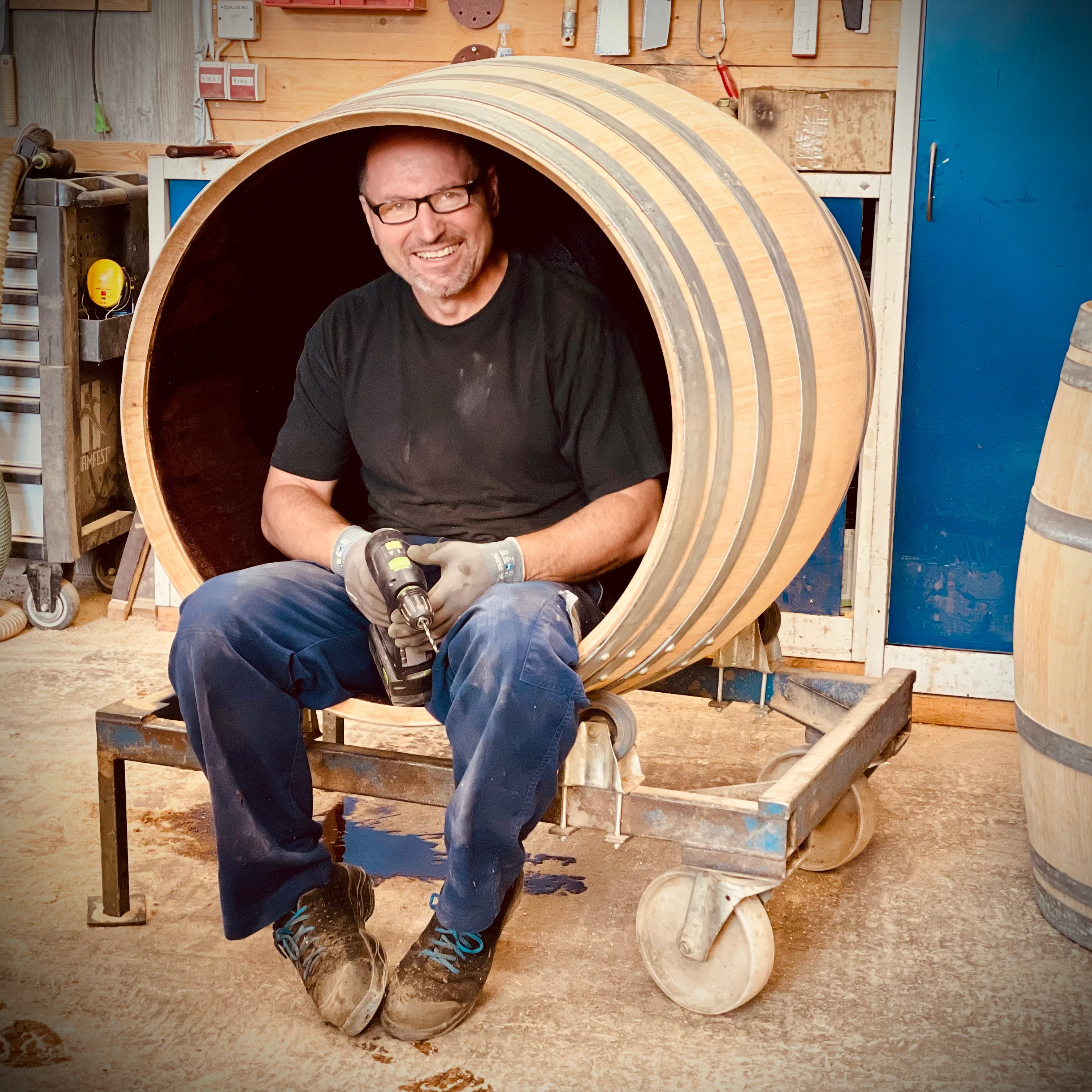Viktor sitzt in einem großen Holzfass in der Werkstatt